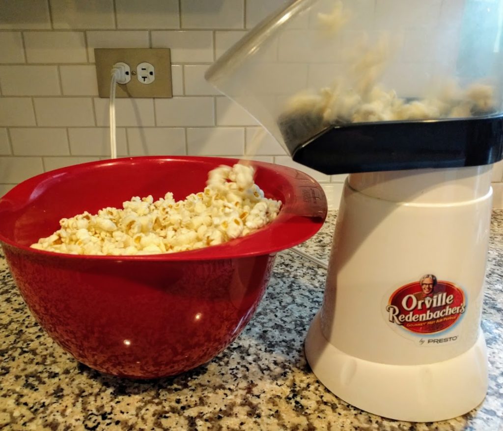 red bowl filled with popcorn sitting next to an air popper