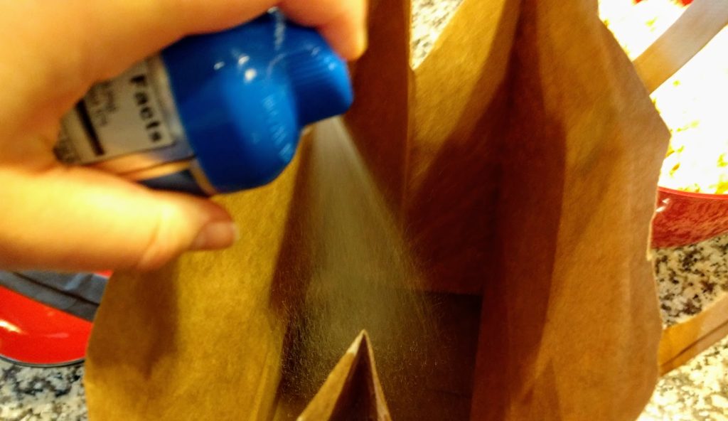hand spraying cooking spray into brown paper bag
