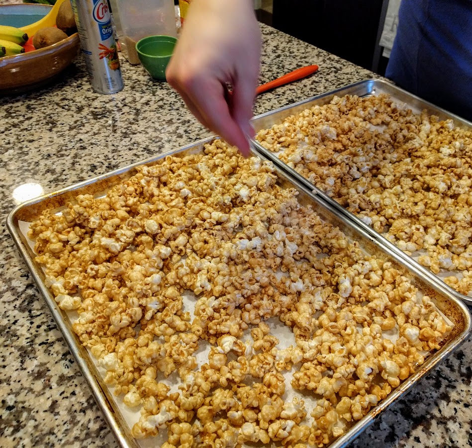 hand sprinkling salt over two baking trays of salted caramel popcorn