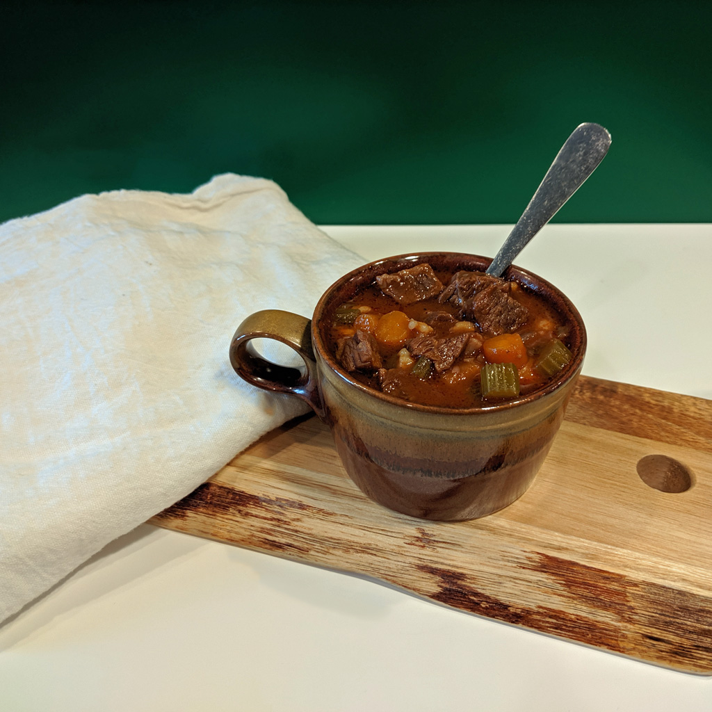 brown mug filled with beef barley soup and a spoon