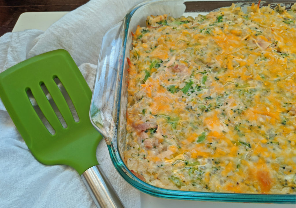a green spatula next to a glass baking dish filled with cooked lightened up broccoli chicken and rice casserole