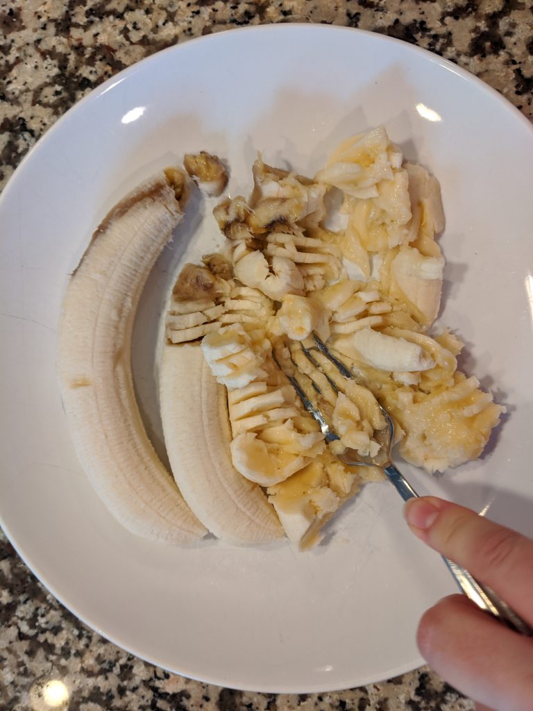 plate with 3 bananas being mashed with a fork