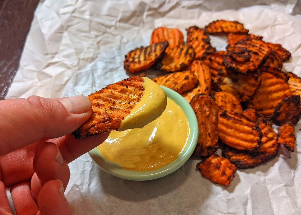 hand holding a fiesta ranch carrot chip dipped in vegan queso style dip