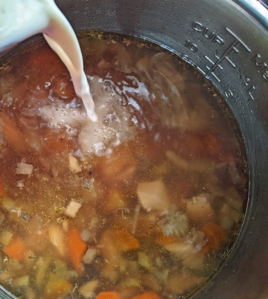 white liquid being pouring into instant pot of hot soup